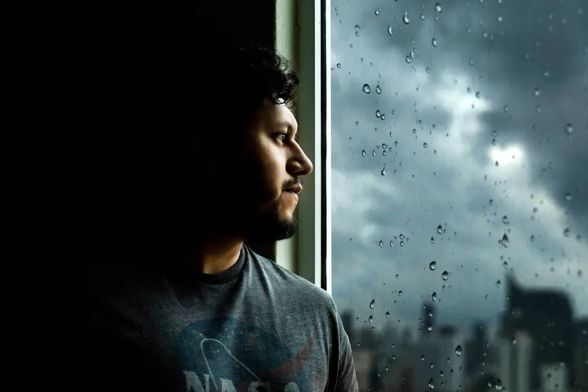 Hombre pensativo mirando por la ventana en un día de lluvia